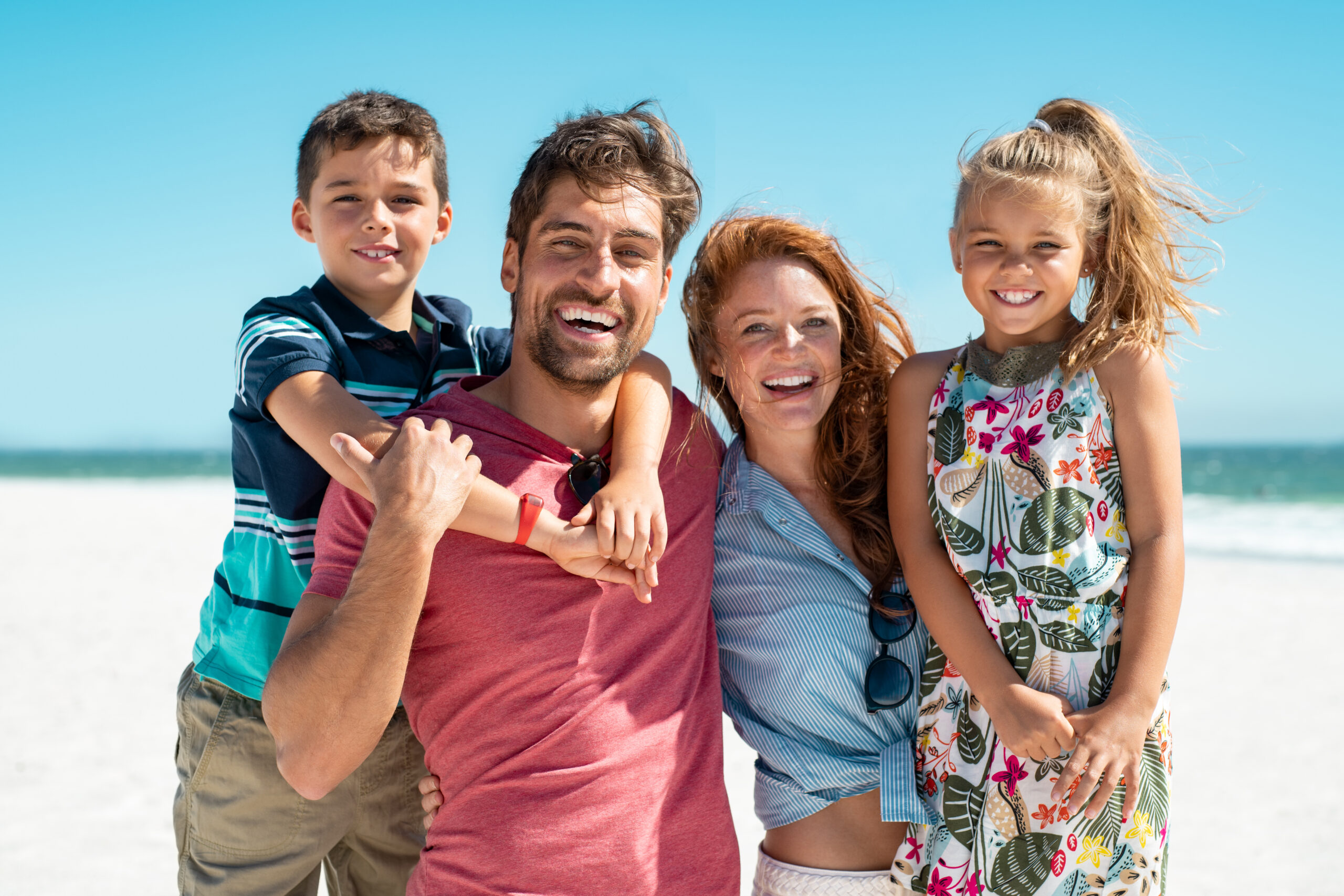 Portrait of happy family looking at camera at beach on a sunny day. Cheerful mother and father with cute daughter and son at sea during weekend. Smiling family with two children enjoying vacation at beach.